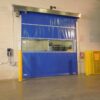 Blue high-speed industrial door with clear viewing panel and safety guards