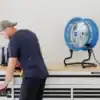 Blue fan on work bench pointing at a man pulling out drawers on the work bench
