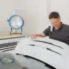 Blue fan on worktable while man works on car